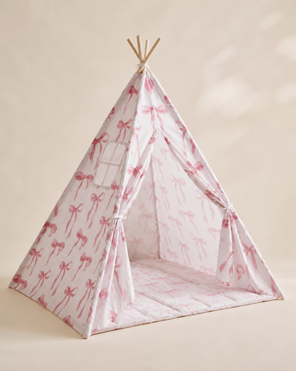 Pink patterned kids teepee tent with bow details on a warm studio background