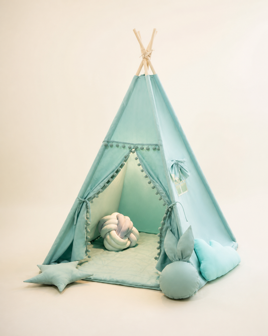 Sage green kids teepee tent with pom-pom trim on a warm studio background