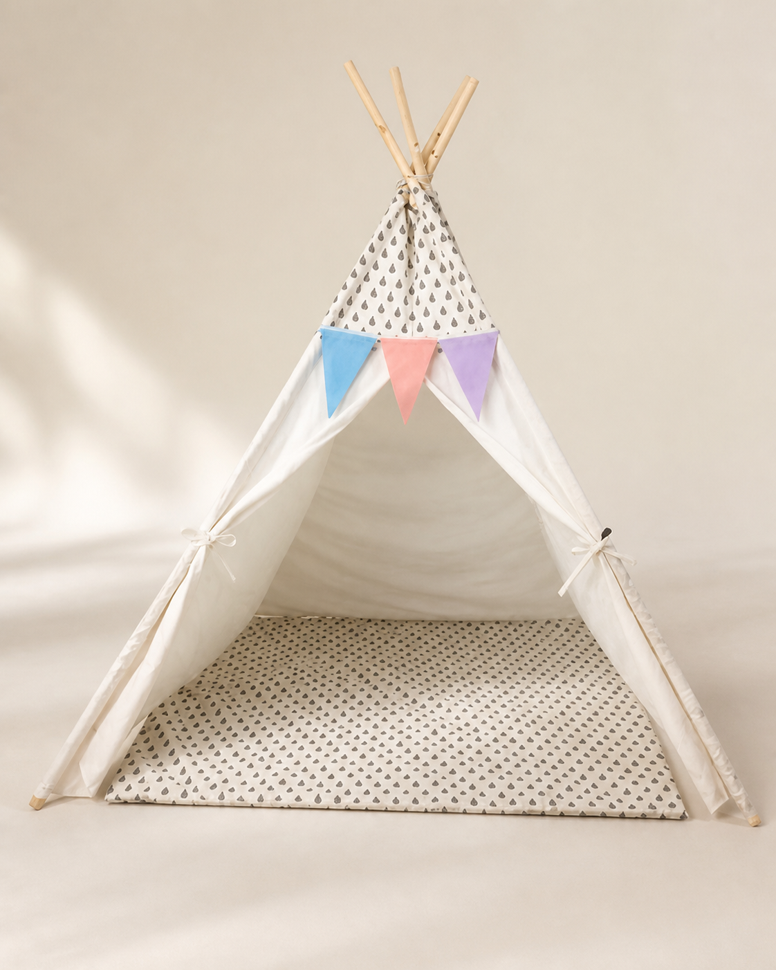 White polka-dot kids teepee tent with pastel bunting and padded mat on a warm studio background